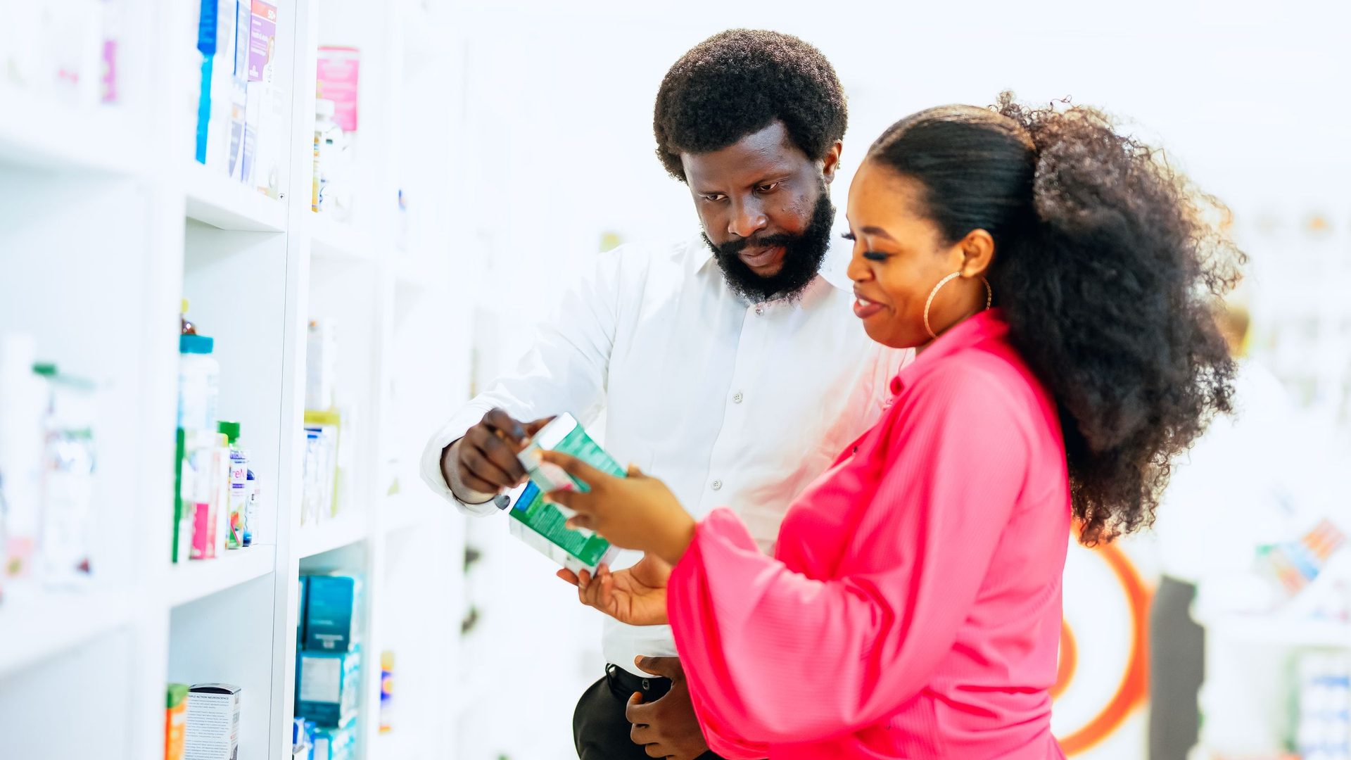 Dans une pharmacie de Lagos, un homme et une cliente regardent ensemble une boîte de médicament devant les rayons.