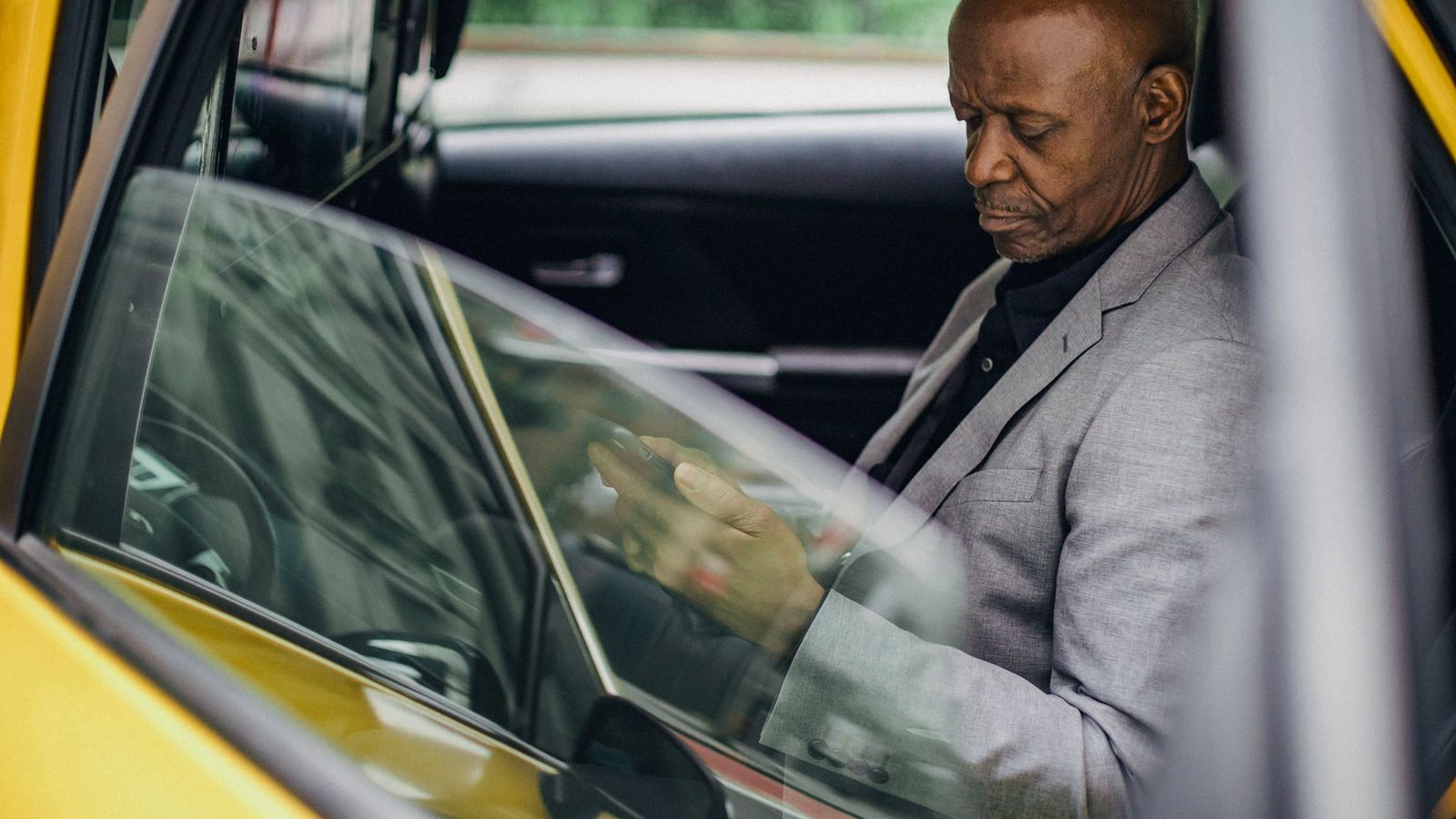 Un homme en veste, assis dans une voiture, consulte son téléphone.