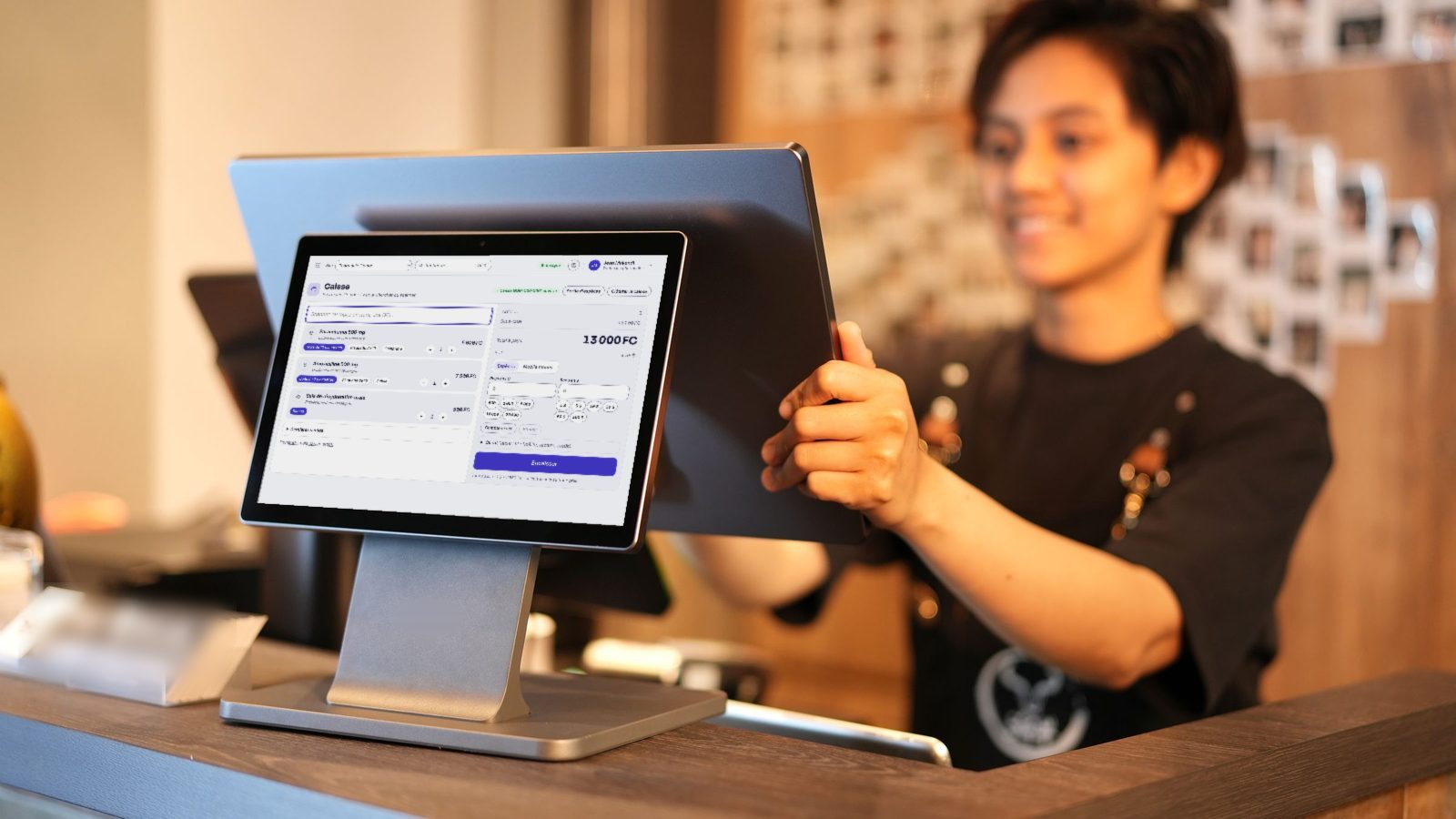 Une caissière encaisse sur une tablette de caisse qui affiche la caisse Vimpia, posée sur le comptoir.